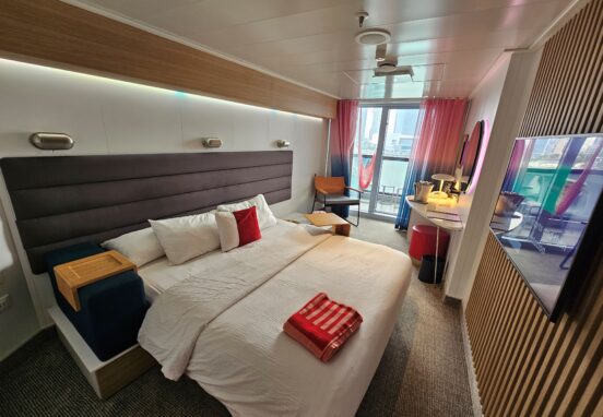 a sea terrace room category on scarlet lady virgin voyages cruise ship showing bed, balcony with hammock, desk space, and tv