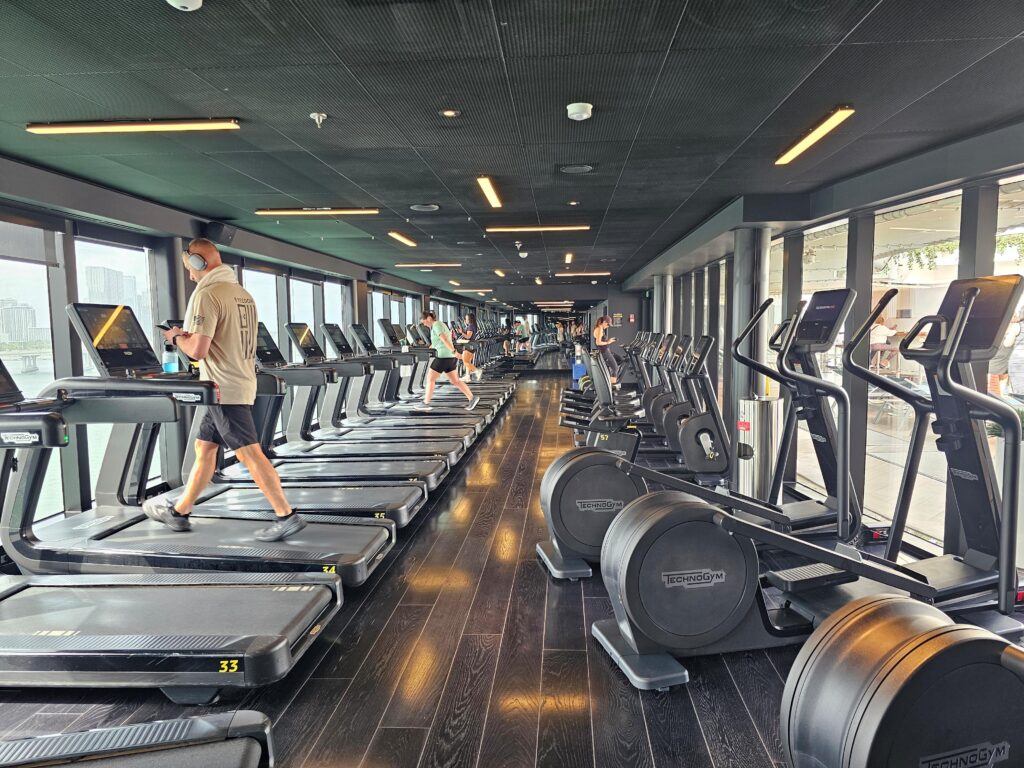 a row of cardio equipment in the gym on scarlet lady virgin voyages cruise ship including treadmills and stationary bikes and elliptical