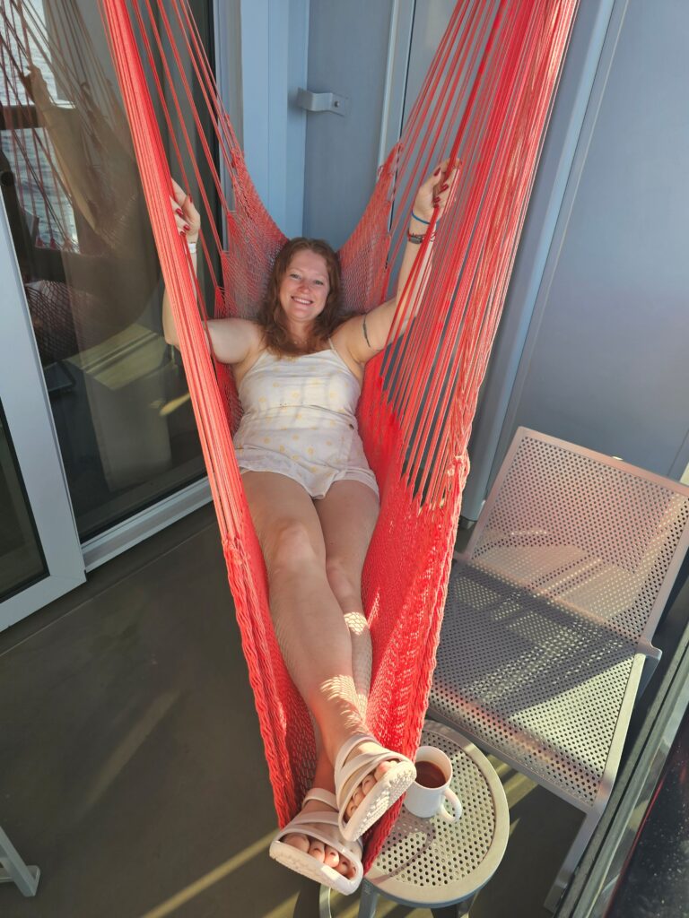 a woman is sitting on a hammock on a cruise ship balcony scarlet lady virgin voyages 