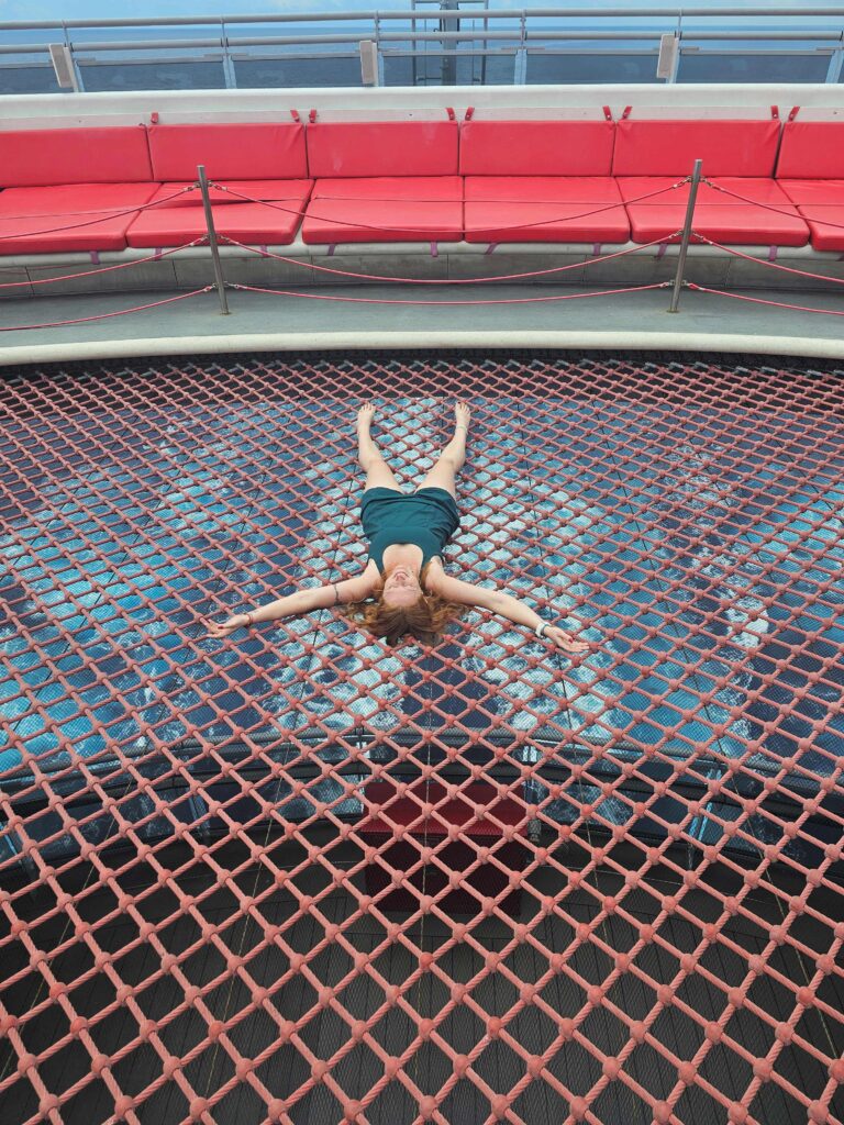 a woman is laying on a net on a cruise ship that is over the ocean below