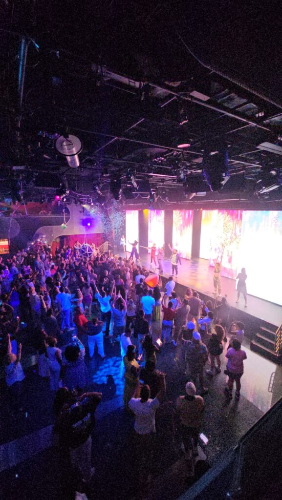 a crowd of people at the y2k party on virgin voyages scarlet lady cruise ship with lights and confetti