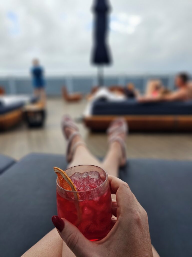 sitting with a glass of sangria on a lounge chair on the deck of scarlet lady ship