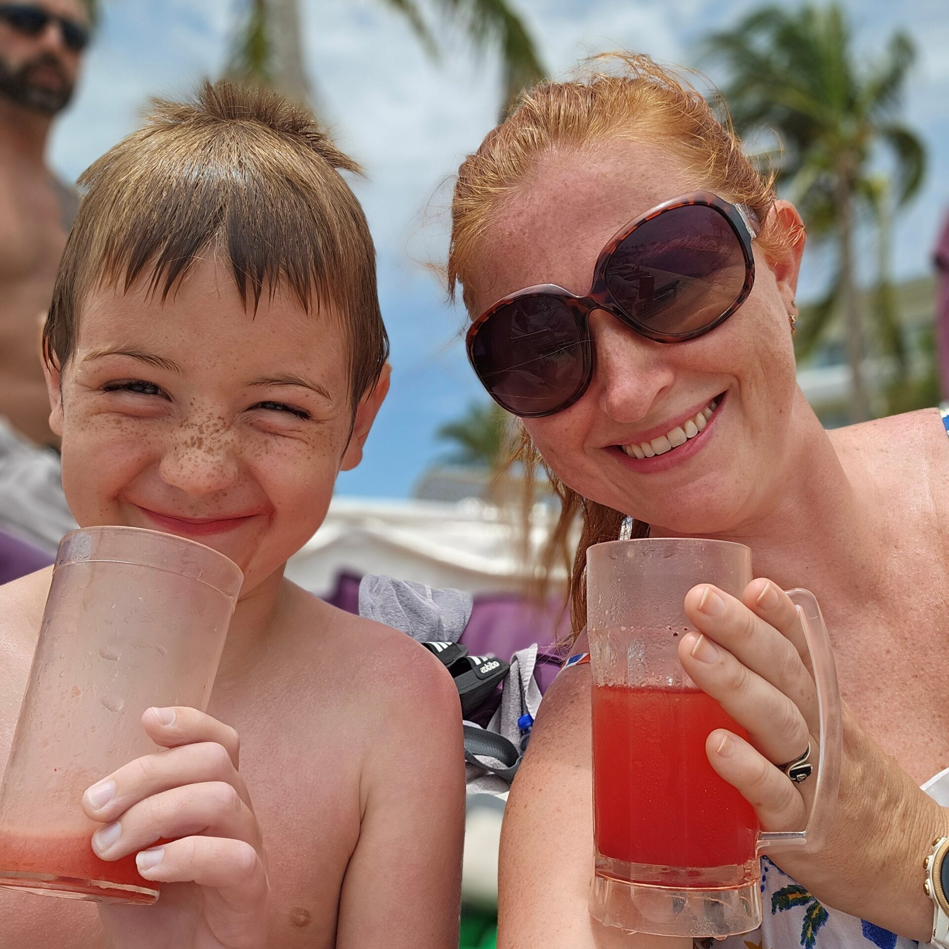 A red haired woman in sunglasses and a blonde haired young boy enjoying brightly colored frozen drinks by the pool at planet hollywood cancun 